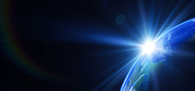 A view of the Earth from space with the sun just rising over the edge with a bright flare.